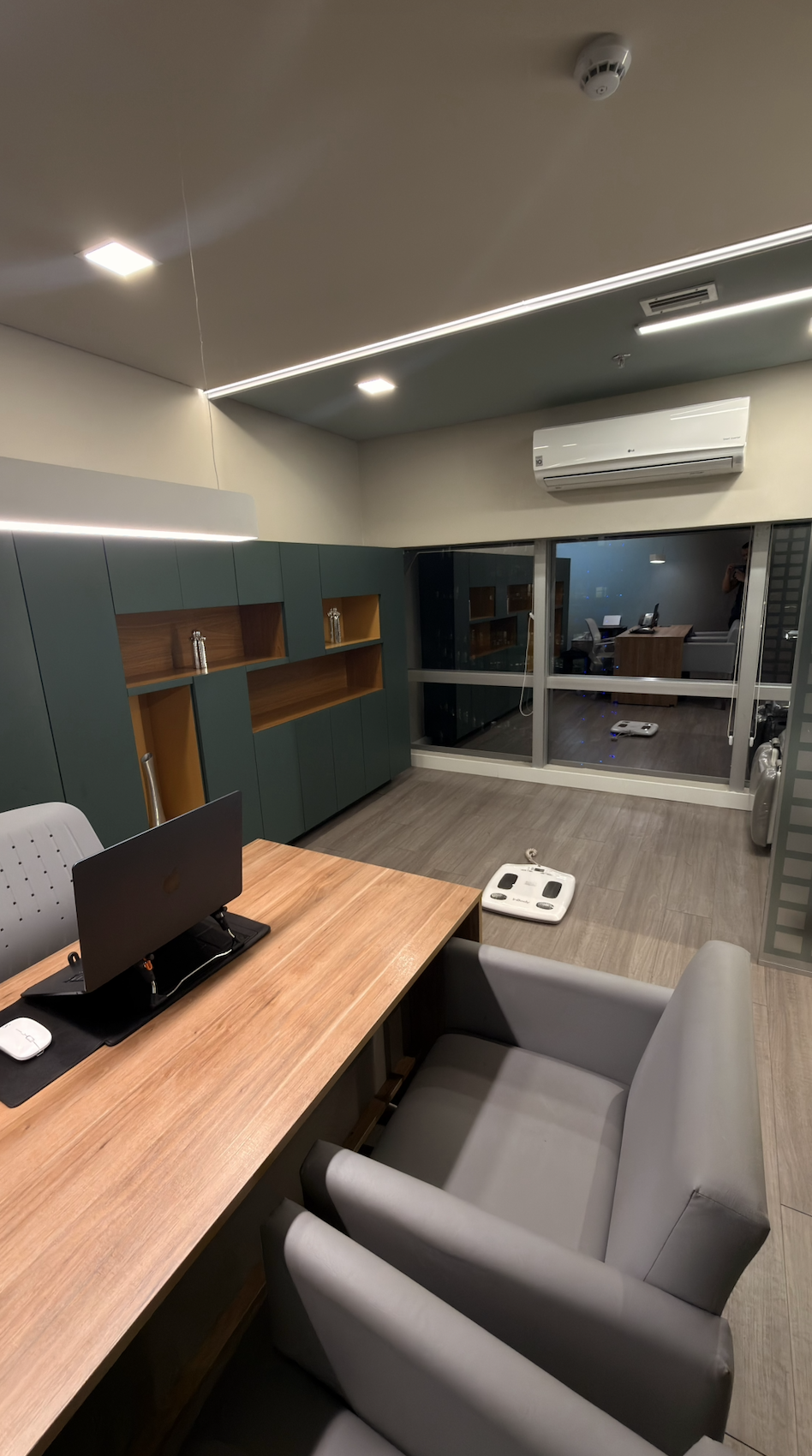 Sala de atendimento do consultório com mesa de madeira, poltronas e equipamento de bioimpedância no piso.